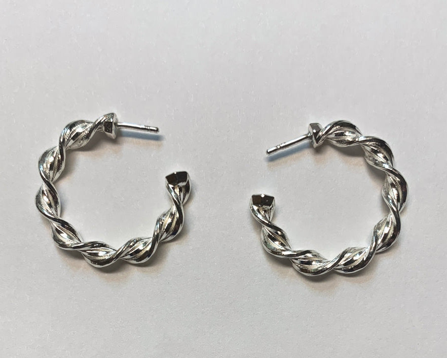 A pair of Hexspiral Hoop Earrings lie on a white surface. 