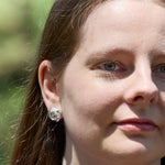 A closeup of the right side of a model's face as she looks off above the camera. She's wearing a pair of Aperture Earrings. 