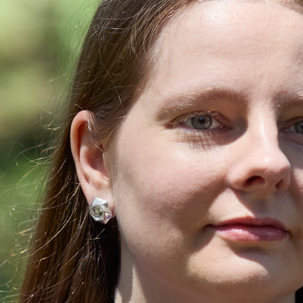A closeup of the right side of a model's face as she looks off above the camera. She's wearing a pair of Aperture Earrings. 
