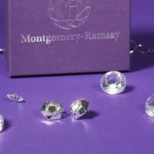 Load image into Gallery viewer, A pair of Aperture Earrings sit on a purple table. In the background is a purple Montgomery-Ramsay product box, and there are some clear gems scattered about. 
