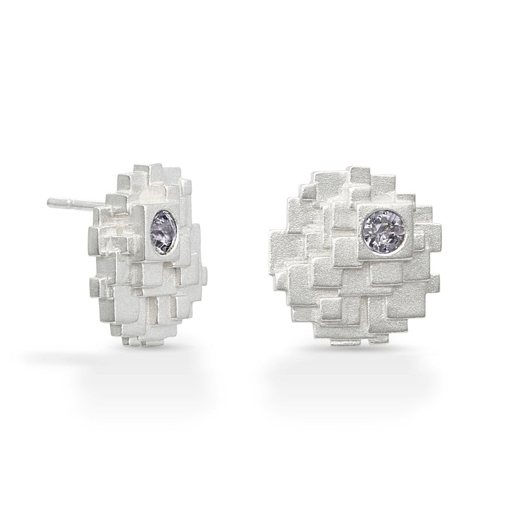 A pair of Geode Earrings on a white background. The Geode Earrings are roughly circular in outline, made up of many different levels of squares stacked over each other. Off-center on each earring is a titanium spinel gem. The two sides are mirror images of each other. 