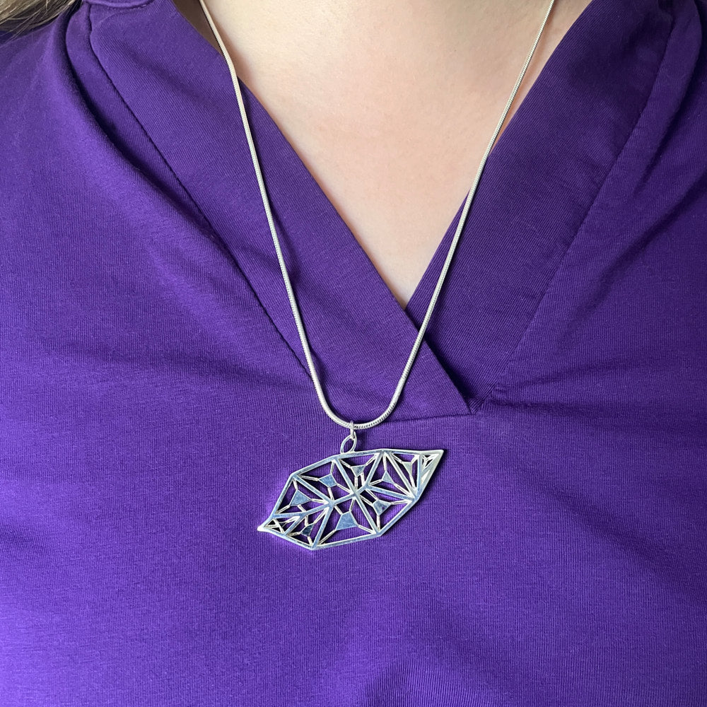 A LīF Necklace hangs from the neck of a model across a purple top. 