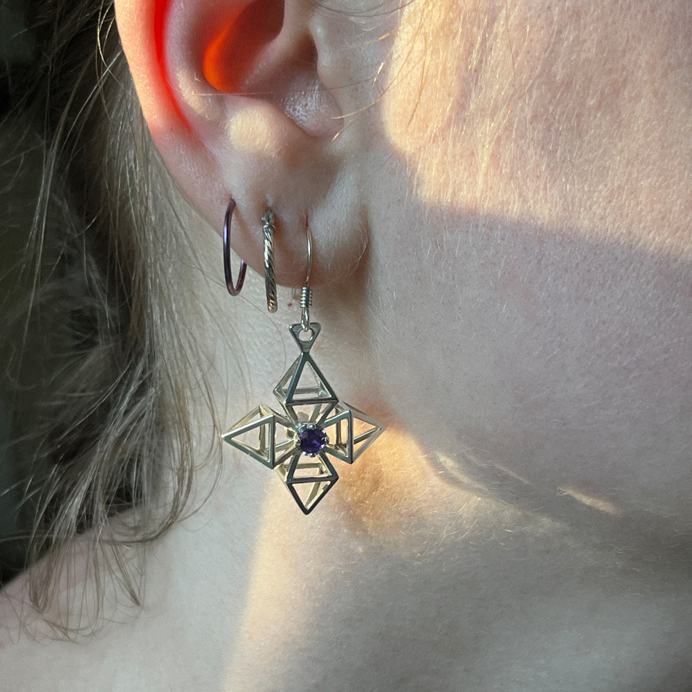 A closeup of a model's ear. One of the Pyrametry earrings hangs down from her earlobe. 