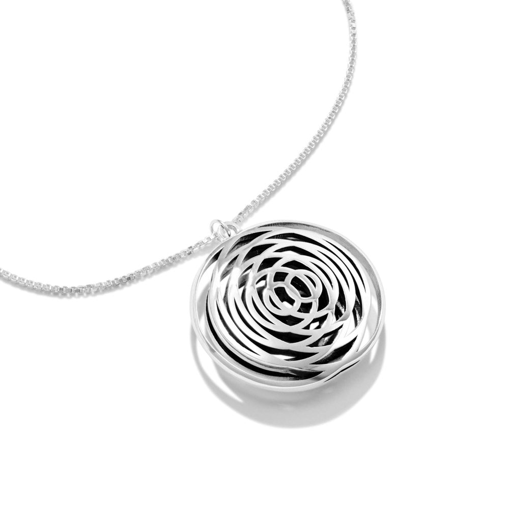 This is a phot of the Intererence Necklace, an ode to the rhythmic beauty of interference waves. Like ripples in a pool, the dual rings of silver radiate outward from the center, colliding and combining to form a mesmerising pendant. At just under 30mm wide and tall, and a full 10mm thick, this is beautifully large pendant to behold from any angle. Hanging from a beautiful 22 inch, 1.5mm box chain, this pendant is precision, beauty, and elegance all wrapped into one.