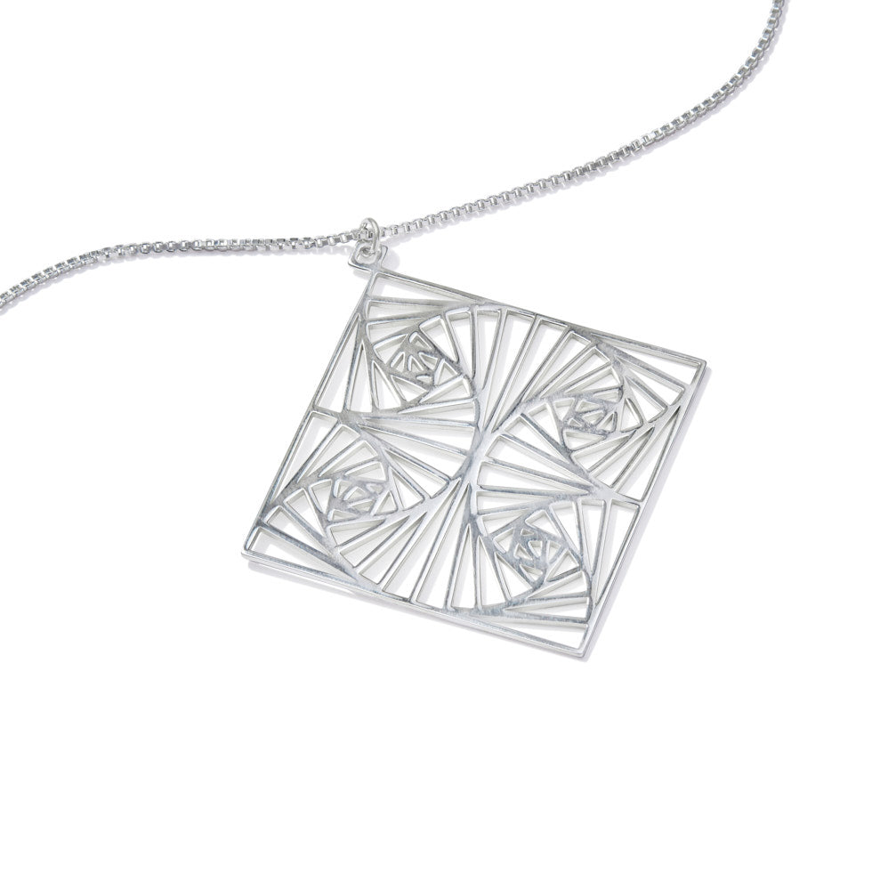 A view of our Square Spiral Medallion at a 45 degree angle over a white background. Inspired by our Square Spiral Earrings, this rather large medallion features a square spiral motif in a repeating pattern, designed with perfect angles at every turn. As about 60mm square, this is a BIG statement piece, but designed to remain lighter than it looks. Hanging from a 22 inch 1.5mm sterling silver Italian box chain, this piece is elegant, powerful, and sure to make a statement.