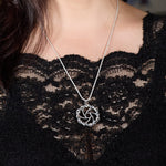The image shows a close-up of a model wearing a black lace top. The focus is on the Maelstrom Necklace she is wearing. The necklace hangs on a rope chain, complementing the pendant. The background is blurred, emphasizing the necklace and the lace top. The overall aesthetic is elegant and sophisticated.
