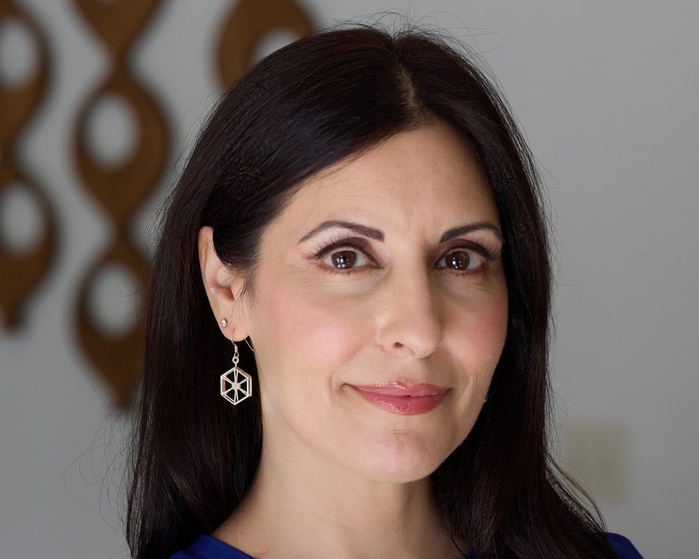 A brunette model wearing a pair of Facet Earrings. Her head is turned just a bit to the side to see the earring hanging from her ear. The background is blurred. 