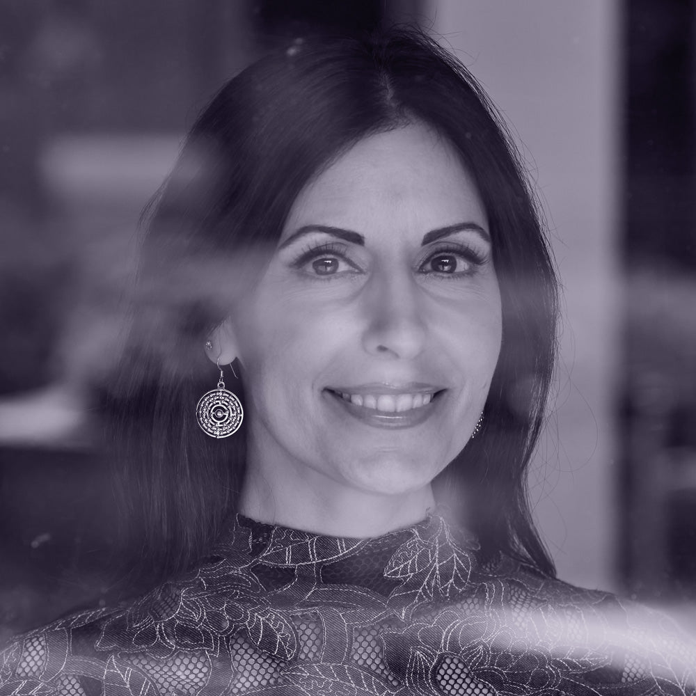 A monochrome image taken through a window of a model wearing the atom earrings. The model is a brunette with shoulder-length hair, and is smiling at the camera.