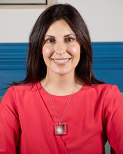Load image into Gallery viewer, A smiling, brunette model wearing our Sunburst Necklace. The necklace hangs over her red shirt. Background is indoors, but blurred. 

