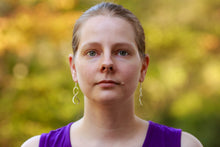 Load image into Gallery viewer, A photo of a model wearing our Ribbon Earrings. This is taken from the front, showing both earrings hanging from the model&#39;s ears. The background is blurred. 
