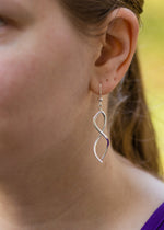 A photo of a model wearing our Ribbon Earrings. This is a closeup of the left side of the model's face, spotlighting the earring hanging from her ear. It is taken from an angle off to the side. 
