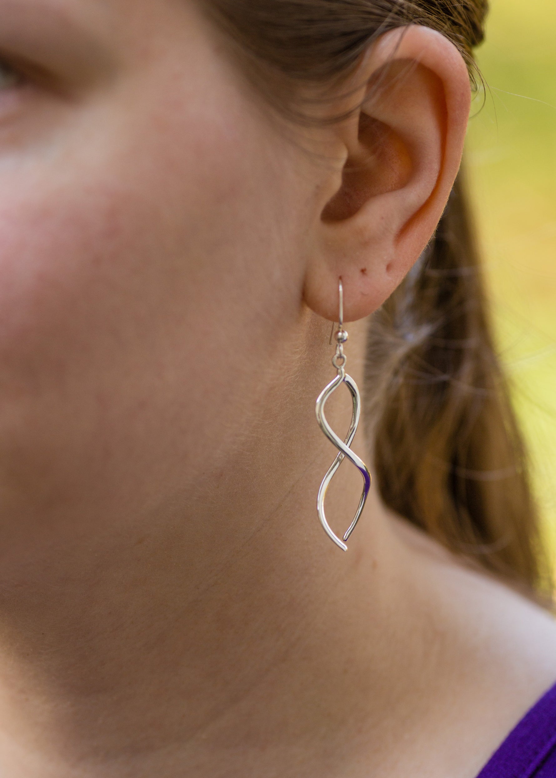 A photo of a model wearing our Ribbon Earrings. This is a closeup of the left side of the model's face, spotlighting the earring hanging from her ear. It is taken from an angle off to the side. 