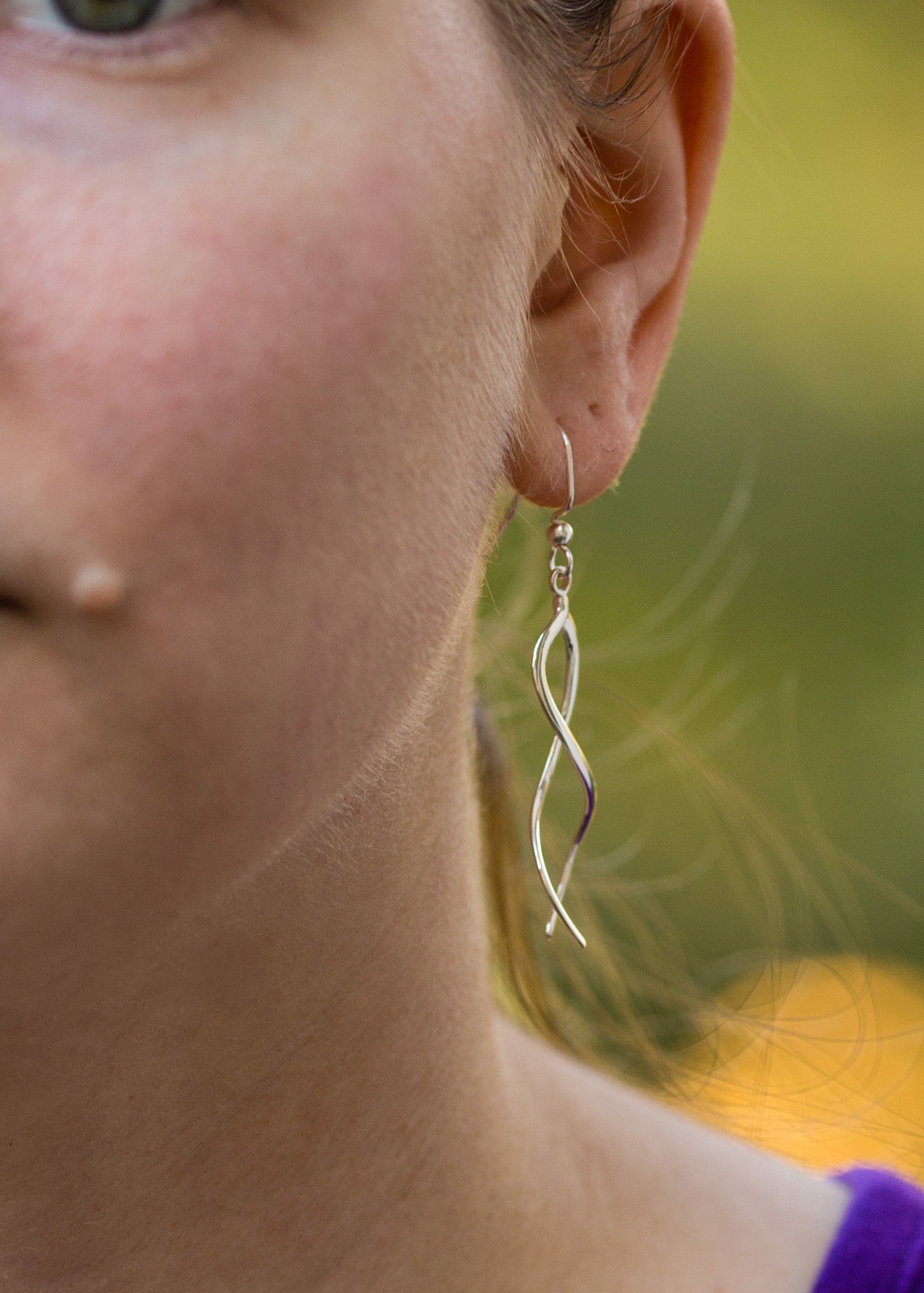 A photo of a model wearing our Ribbon Earrings. This is a closeup of the left side of the model's face, spotlighting the earring hanging from her ear. It is taken from the front. 