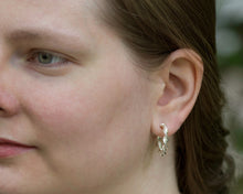 Load image into Gallery viewer, A model wears the Hexspiral Hoop Earrings. The model is looking off to the left of the frame, and the focus is on the earring in her left ear. She is outdoors. 
