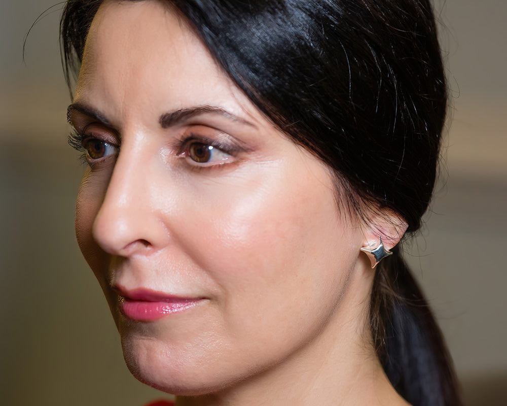 A photo of a brunette model wearing our Folded Square earrings. The photo is a closeup of the left side of the model's face, focusing on the earring.