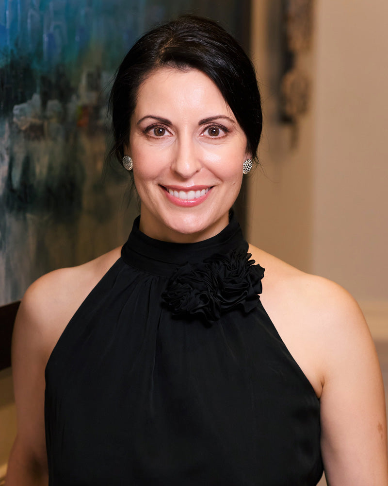 A photo of a smiling, brunette model wearing our Beehive Earrings. The model is in a black top and the photo is taken indoors. 