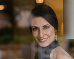 A photo through a window of a smiling brunette model wearing our Double Spiral Earrings. 