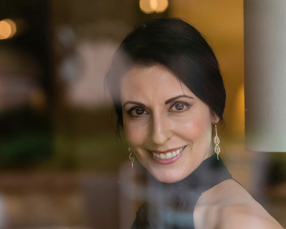 A photo through a window of a smiling brunette model wearing our Double Spiral Earrings. 