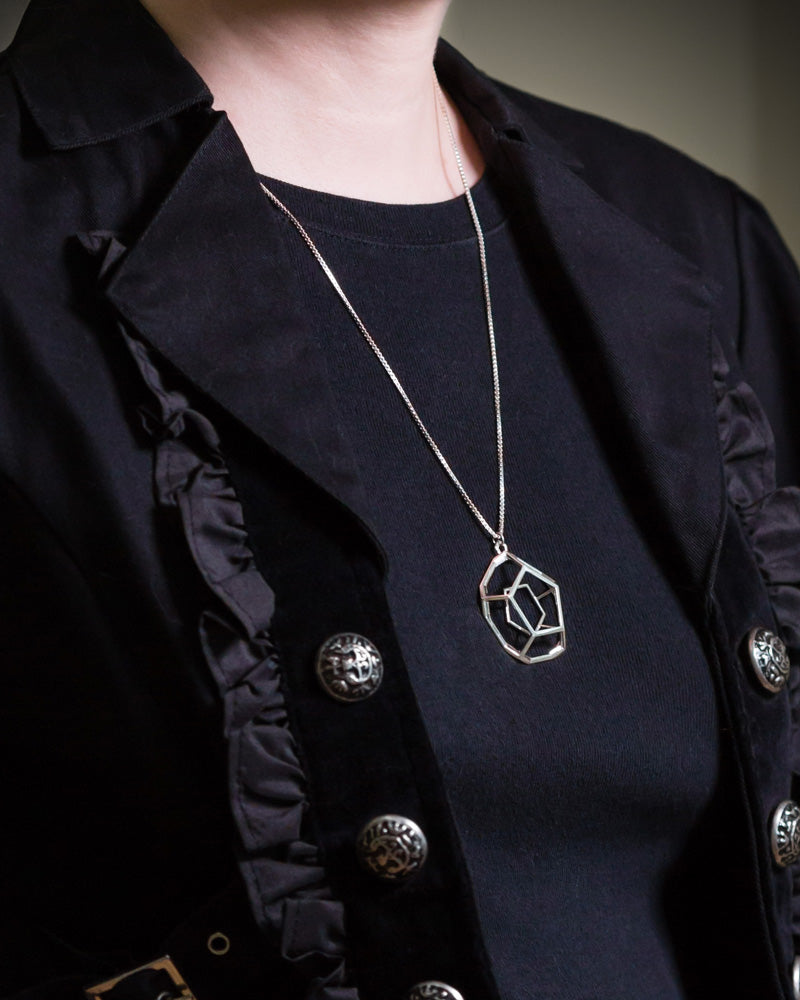 A photo from a 45 degree side angle of a model wearing our Dodecahedron Necklace. The model is in black. 