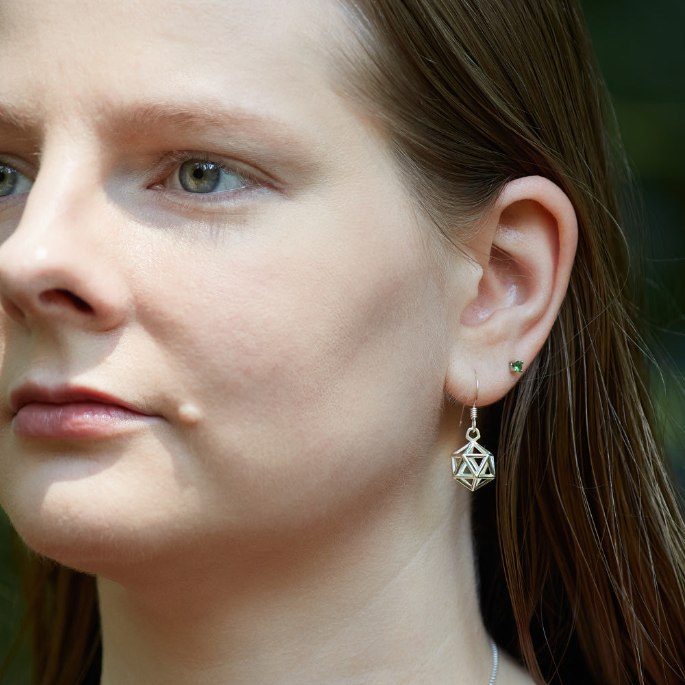 A young blonde model wears a pair of D20 Earrings outdoors in the sun. The image is a view looking toward her left ear as she looks off to the left of the frame. The D20 Earring hangs down, reflecting the sunlight. 