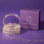 A photo of a stack of Scaffold Bangles sitting next to a Montgomery-Ramsay product box. The table and background are both purple, and there is a hexagonal sterling silver chain trailing around in the foreground and background. 