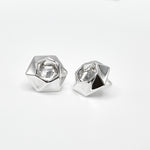 A pair of sterling silver Aperture Earrings against a white surface. The earrings feature a twisty hexagonal design, and measure about 15.7mm from flat to flat. At 7 grams each, they're eminently comfortable to wear, but still make a bold statement. 
