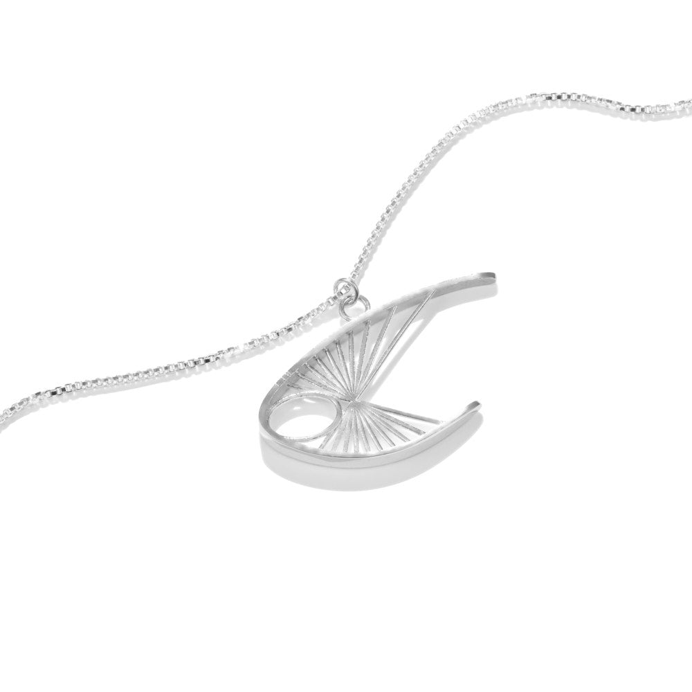 The Curlew Necklace lies on a white background at a slight angle. The pendant is a piece inspired by the Curlew stringed figure sculpture from Barbara Hepworth, itself named for the curlew bird. Growing up, it was a prominent piece in the collection of Neil Ramsay's parents, and has been an inspiration for a great many ideas in the Montgomery-Ramsay jewellery line. This elegant shape in sterling silver hangs from a point along the center of mass that ensures its proper upswept angle.