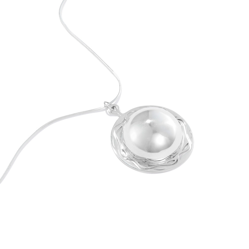 A product photo of our Scrying Pool Necklace, lying at an angle on a white table. The necklace is a half dome of silver, shined to a mirror polish, and surrounded with a frame of silver sporting ripple designs. 