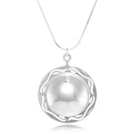 A product photo of our Scrying Pool Necklace, hanging in front of a white background. The necklace is a half dome of silver, shined to a mirror polish, and surrounded with a frame of silver sporting ripple designs. 