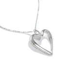 A production photo of our Heart of Hearts Necklace at a 45 degree angle, lying on a white surface. The Necklace is a large, heart shape, empty in the center, with a heart shaped bail and heart cutouts around the edge.