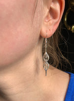 A photo of a young blonde model wearing our Double Spiral Earrings. The photo is a closeup of the model's left ear, showing the earring dangle down her neck.