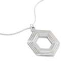 A Stepped Hexagon Necklace lies on a white surface at a 45 degree angle. This large sterling silver necklace is a statement piece, comprised of a modern geometric design featuring rising and falling levels of hexagons. Part of our Stepped Hexagon collection.
