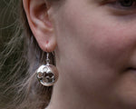 A closeup of our Cross Ball Earrings hanging from the ear of a model, taken from a 45 degree angle toward the front. 