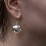 A closeup of our Cross Ball Earrings hanging from the ear of a model, taken from the side. 