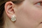 A photo of a young blonde model wearing our Moonscape Earrings. The photo is a closeup of the model's right side, focusing on the earrings. 