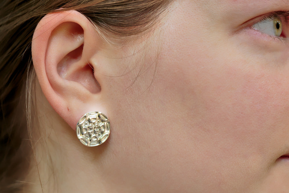 A photo of a young blonde model wearing our Moonscape Earrings. The photo is a closeup of the model's right side, focusing on the earrings. 