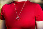 A photo of our Heart of Hearts Necklace around the neck of a model. The model is wearing a red shirt, and the photo was taken outdoors in the sunlight. 