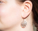 A photo of a blonde model wearing our Supernova Earrings. The photo is a closeup of the model's face on her left side, with the earrings in focus. The photo was taken outdoors in the sun. 