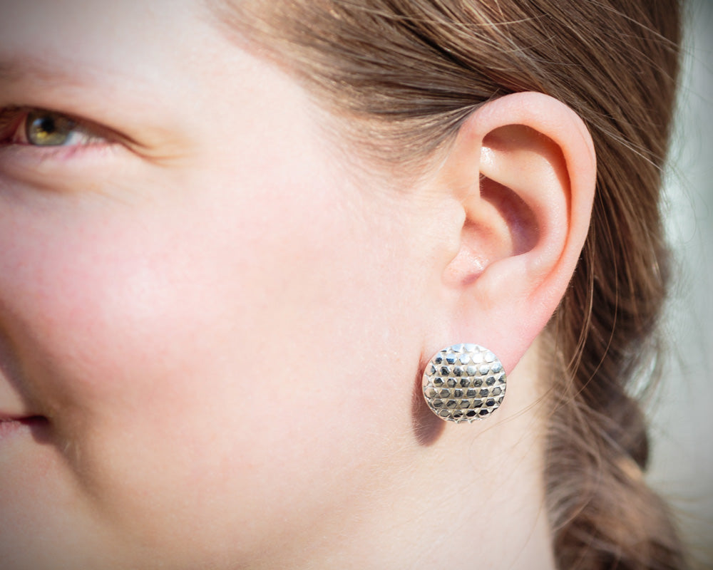 A photo of a model wearing our Beehive Earrings. The photo is a closeup of the earring on the model's ear, taken outdoors in the sunlight. 