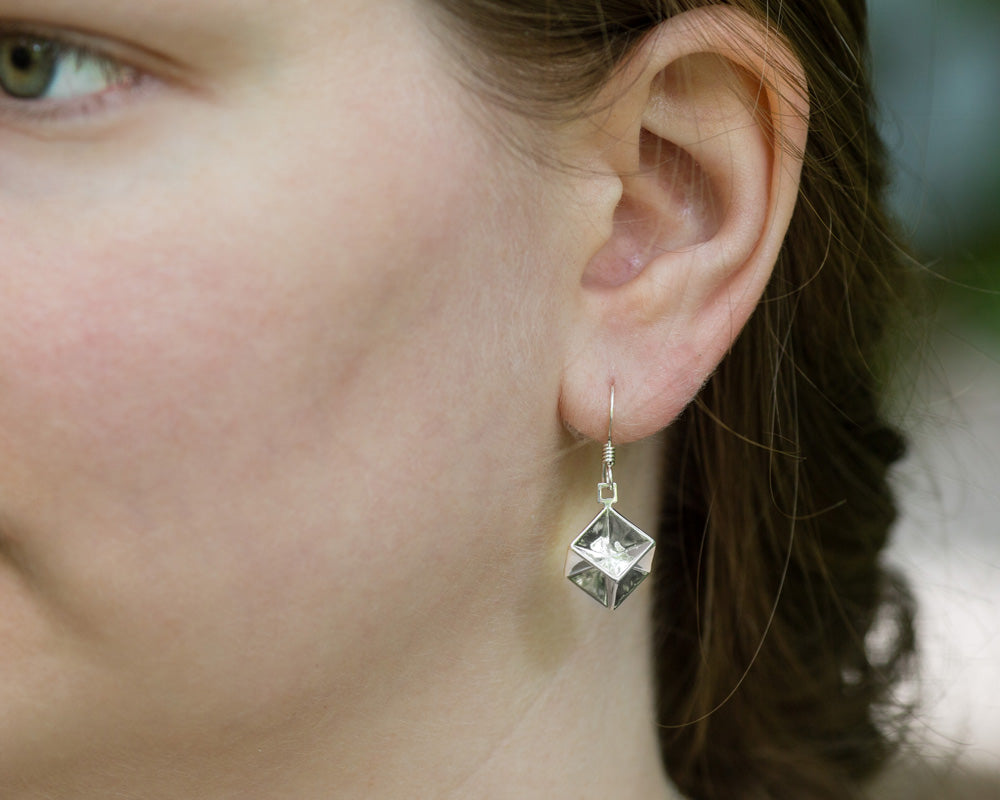 A model wears our sterling silver Tesseract Earrings. This shows a closeup of the earring on the model's left ear. 