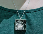 A model wears our Sunburst Necklace outdoors in the sun. The model's face is not shown, and the photo focuses closely on the necklace in center lower frame. It glints in the sunlight. 
