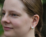 A photo of a young blonde model wearing our Folded Square earrings. The photo is a closeup of the left side of the model's face, focusing on the earring. 