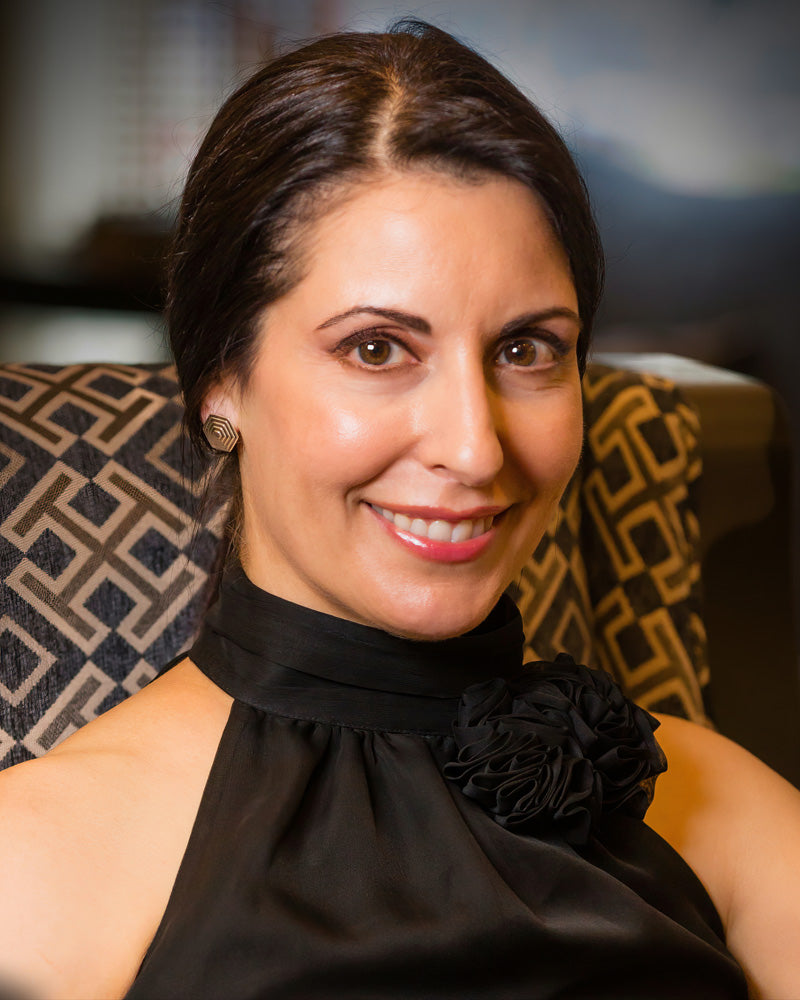 A photo of a smiling brunette model wearing our Hexagonal Pyramid Stud Earrings. The model is wearing a black dress and is looking toward the camera. 
