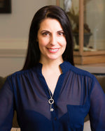 A brunette model in a dark navy shirt is wearing a Celtic Key Necklace. The model is smiling and looking at the camera. The background is indoors, but blurred.